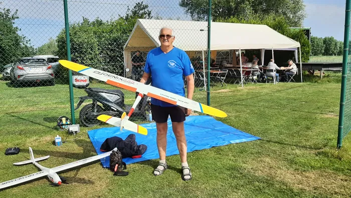 Piloot draagt zijn zweefvliegtuig over het veld, langs de tenten